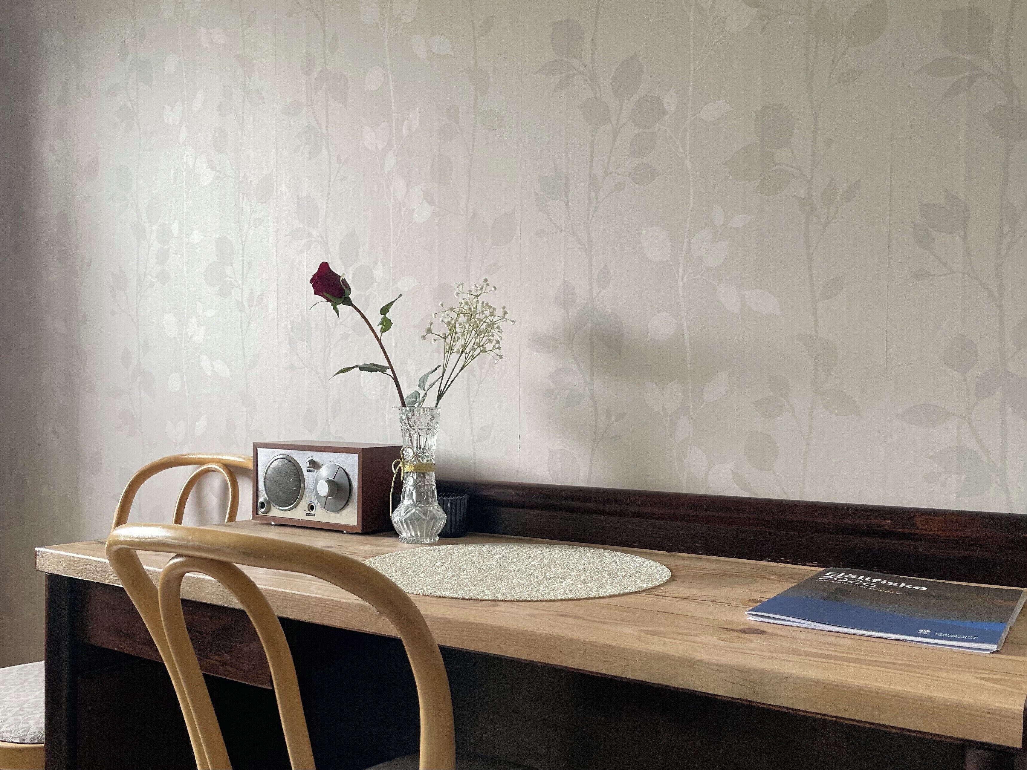 A wooden table with a radio, a vase with flowers, and a book.