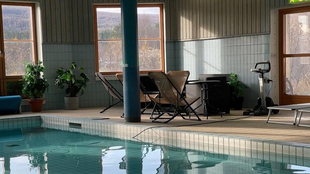 Une piscine intérieure avec un sol carrelé, des chaises, une table et des plantes en pot.