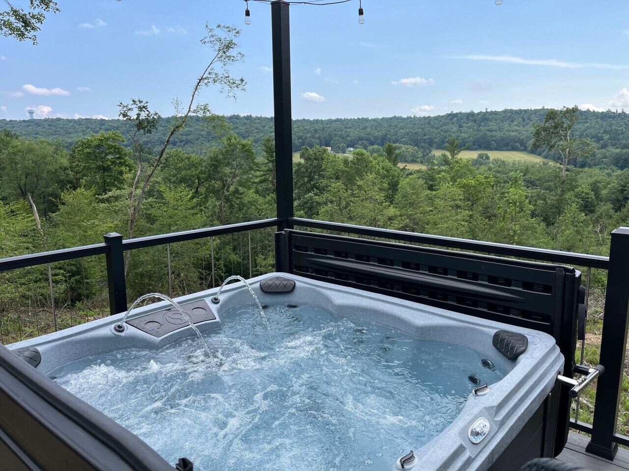 A hot tub on a balcony with a scenic view of a forested hill.