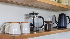 Een keukenschap met een koffiezetapparaat, een French press en twee witte mokken.