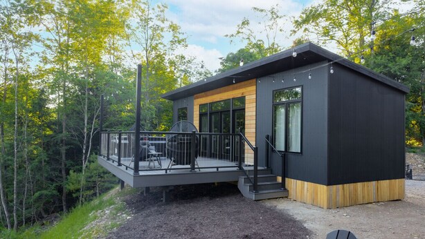 Una cabaña moderna con terraza, rodeada de árboles.