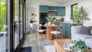 Una cocina moderna con gabinetes azul verdoso, un refrigerador negro y un microondas. Hay un comedor con una mesa y sillas de madera.