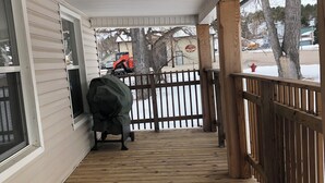 A covered wooden deck with a railing, a covered grill, and a view of a street with a red fire hydrant and a yellow school bus. - Charming 4-bedroom house with WiFi, AC in wonderful Sundance (Sundance)