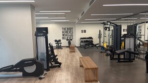 Une salle de sport équipée de divers appareils d’exercice, de bancs en bois et décorée de motifs inspirants sur les murs.