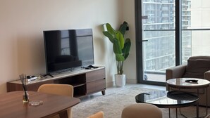 Un salon moderne avec un téléviseur à écran plat posé sur une console en bois, une plante en pot, une table basse ronde et un canapé.