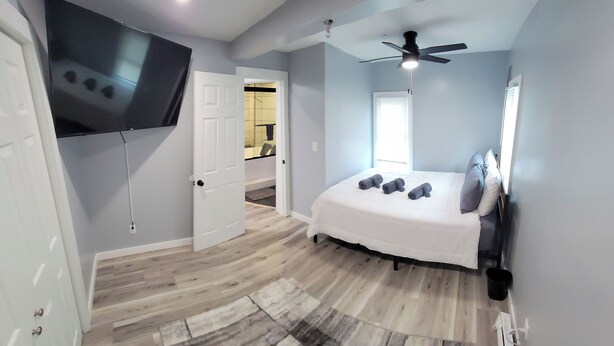 A bedroom with a bed, a ceiling fan, a TV mounted on the wall, and a wooden floor. - GOTL Lovers Chateau Cottage U7 (Geneva)