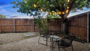 A backyard with a wooden fence, a tree with string lights, a metal table and chairs, and a gravel path. - Exquisite 4 Bed Great Location (Richardson)