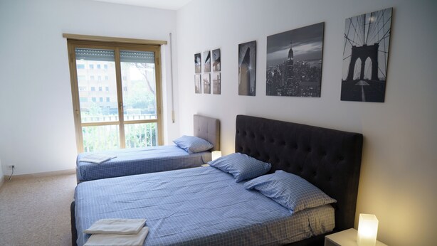 A bedroom with two beds, a window with blinds, and several wall-mounted pictures.