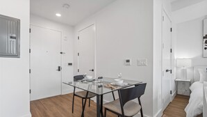 A modern room with a glass dining table, two chairs, a bed, and a bedside table with a lamp. - Chic studio with fitness room, WiFi in delightful Brooklyn (Brooklyn)