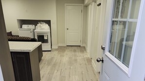 A hallway with a wooden floor leading to a door with a glass panel. A small rug is placed at the entrance. - Cozy Private Oasis Peaceful Stay (Milton)