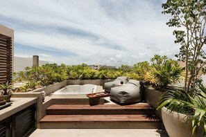 A rooftop patio with a hot tub, outdoor seating, and lush greenery.