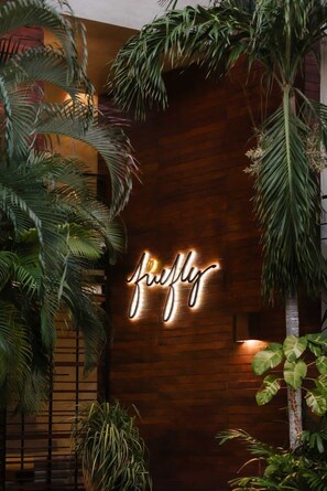 A neon sign with the word 'flying' on a wooden wall surrounded by tropical plants.