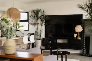 A modern living room with a black entertainment unit, a round coffee table, and a dining area with a white chair.
