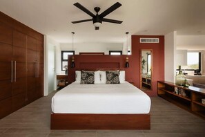A bedroom with a large bed, a ceiling fan, wooden wardrobe, and a view of the outside.