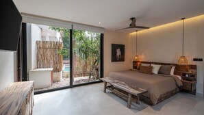 Ein modernes Schlafzimmer mit einem großen Bett, einer Bank und Blick auf einen Bambuszaun und viel Grün außerhalb.