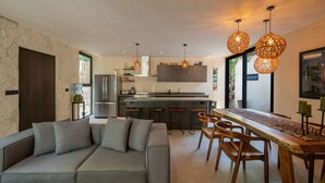 Eine moderne Küche mit grauem Sofa, Esstisch aus Holz und hängenden Pendelleuchten.