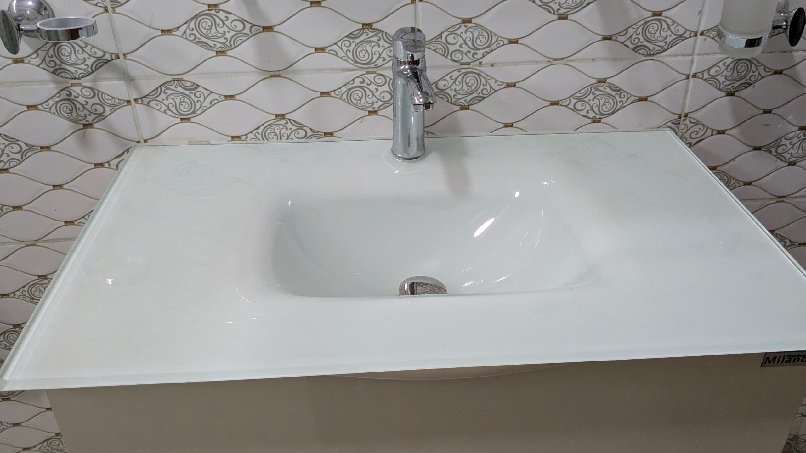 Une salle de bain avec un lavabo blanc, un robinet et un mur recouvert de carreaux décoratifs.