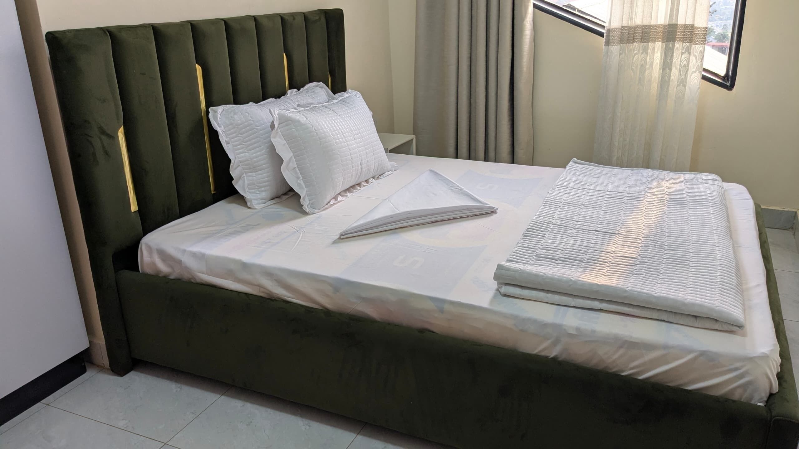 A neatly made bed with white bedding, a green upholstered headboard, and a small bedside table.