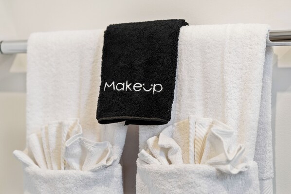 Une salle de bain avec deux serviettes suspendues à un porte-serviettes, dont l’une est brodée du mot « Maquillage ».