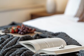 Un livre posé sur une couverture, avec des écouteurs placés sur le dessus, une assiette de fruits et un lit en arrière-plan.