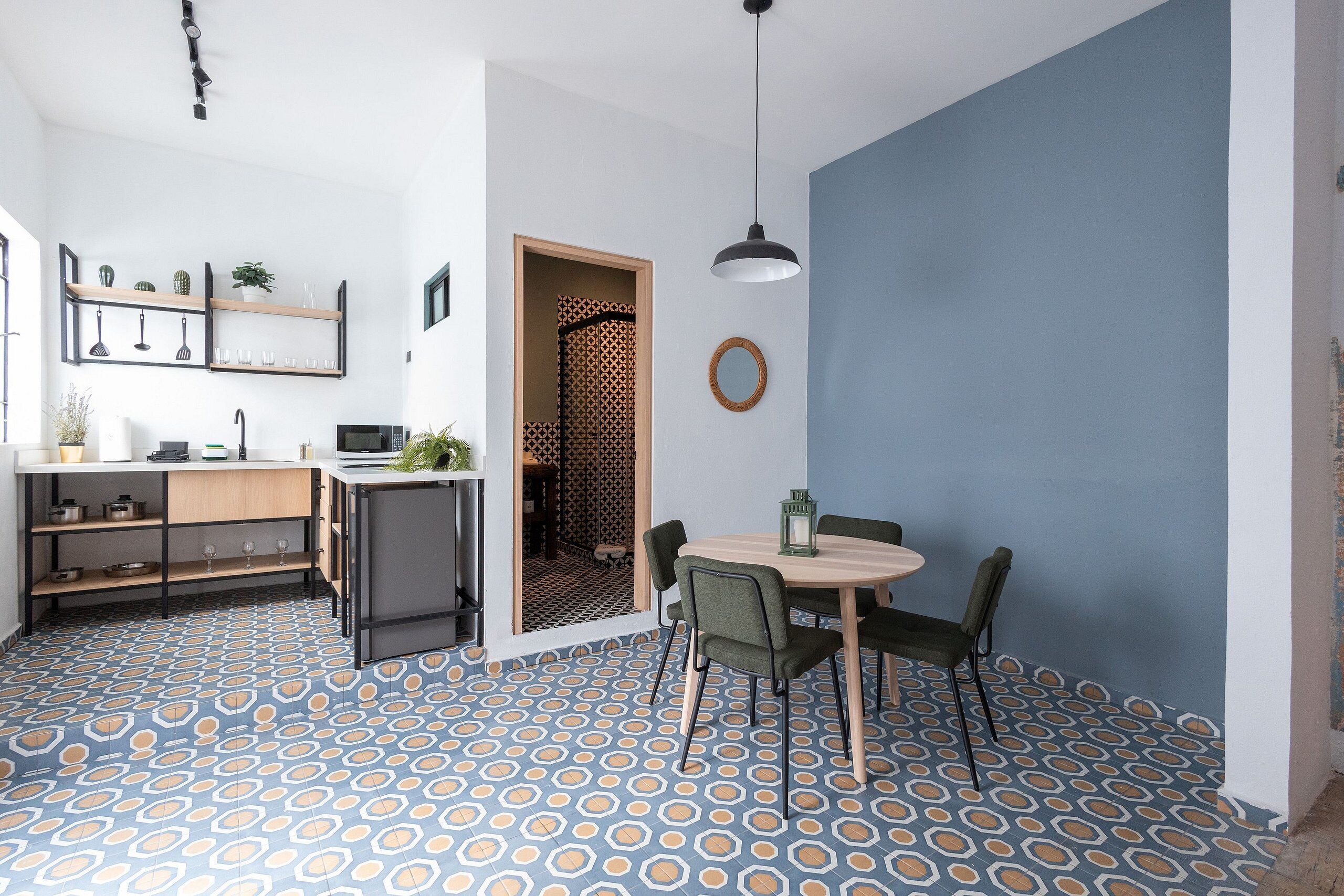 A modern kitchen with a dining area, featuring a patterned floor, wooden furniture, and a pendant light.