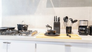 Moderni keittiö, jossa on kaasuliesi, kattiloita, kahvinkeitin ja erilaisia keittiövälineitä työtasolla.