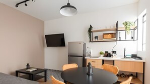 En kompakt bolig med spiseplads, tekøkken og et fladskærms-tv på væggen.