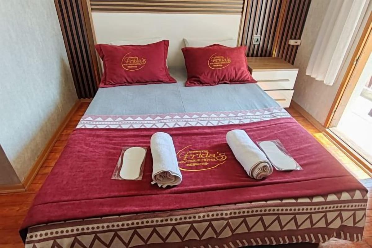 Ein Bett mit einem gemusterten Überwurf, zwei Kissen mit einem Logo und ordentlich gefalteten Handtüchern.