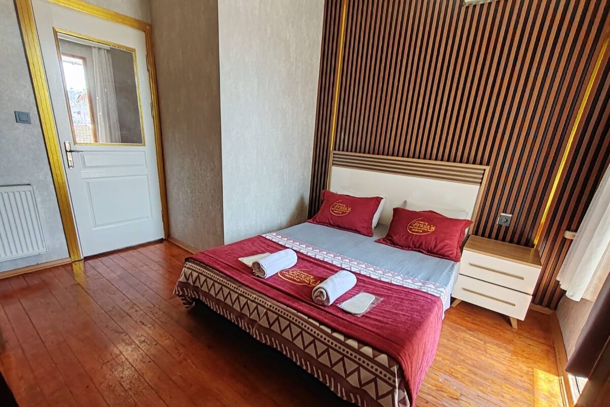 A neatly made bed with a patterned bedspread and pillows, a wooden headboard, and a bedside table with a lamp.
