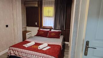 A hotel room with a bed, a bedside table, a window with curtains, and a door.