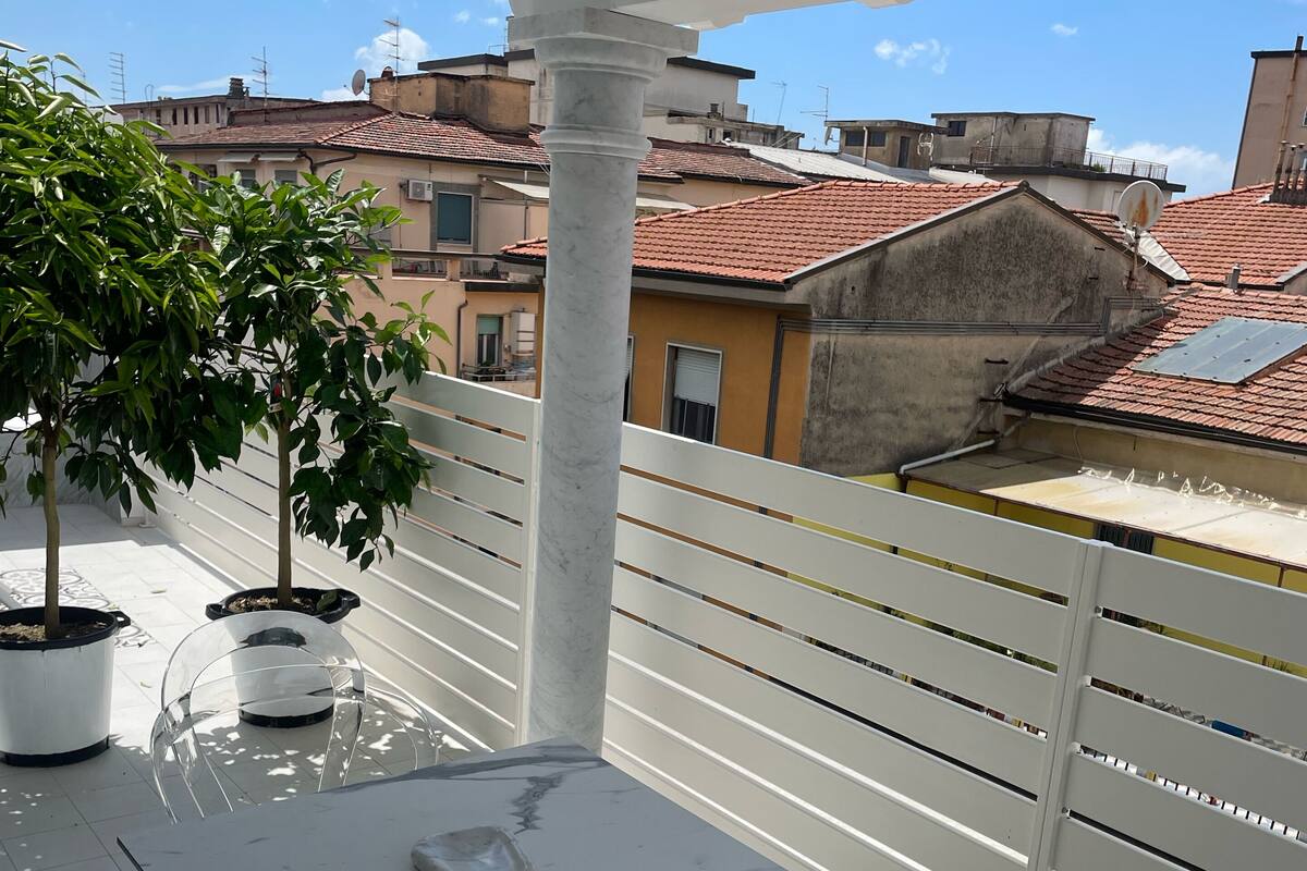 Un balcon avec une balustrade blanche, une table en marbre et deux plantes en pot.
