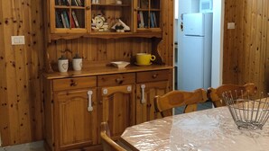 Ein Esszimmer mit Holzboden, einem Tisch, Stühlen und einem Schrank mit Büchern und Geschirr.