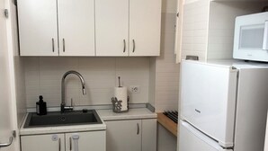 Eine kleine Küche mit weißen Schränken, einer Edelstahl-Spüle, einer Mikrowelle und einem Kühlschrank.
