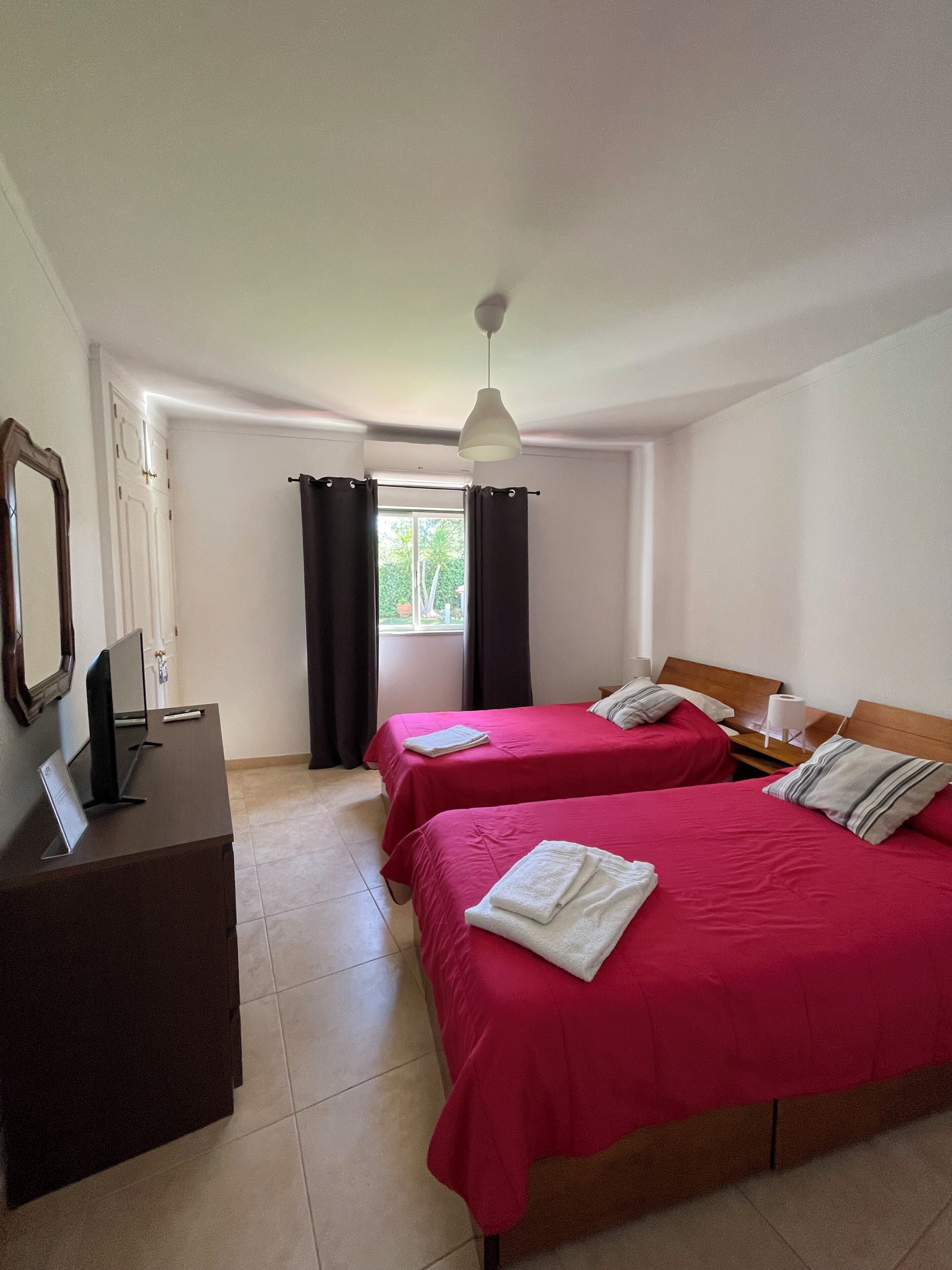 A hotel room with two beds, a desk, a mirror, and a window with curtains.
