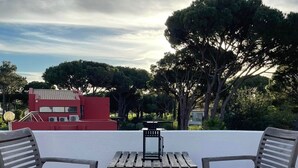En terrasse med to træstole og et lille bord, der kigger ud over en rød bygning og træer.