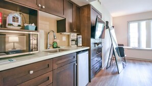 Une cuisine moderne avec des meubles en bois foncé, un évier en acier inoxydable et un four encastré. Une fenêtre laisse entrer la lumière naturelle et offre une vue sur l’extérieur.