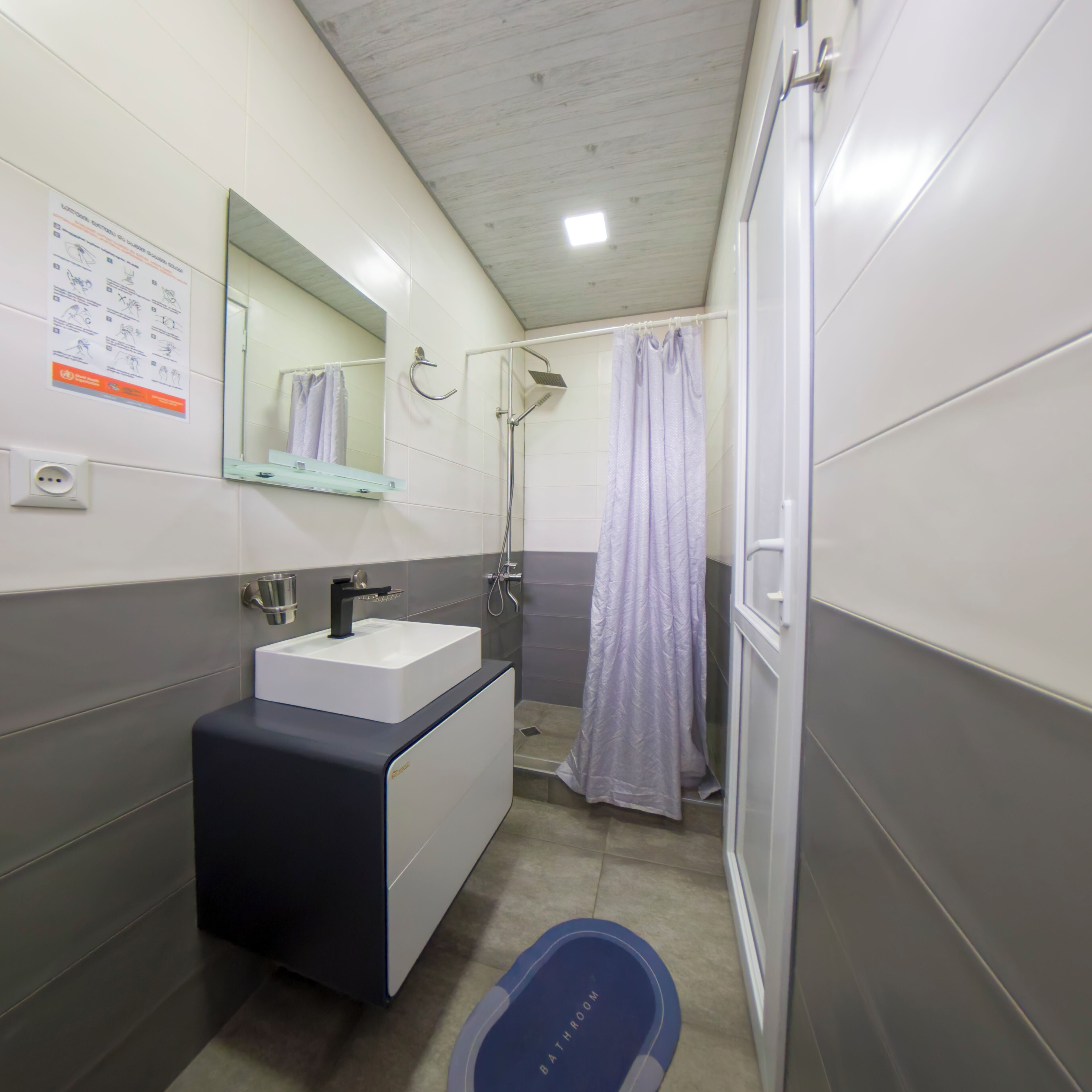 A bathroom with a sink, mirror, shower, and a blue mat labeled "RATATONG."