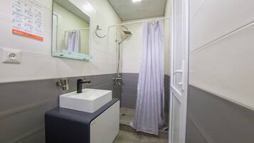 A bathroom with a sink, mirror, shower, and a blue mat labeled "RATATONG."