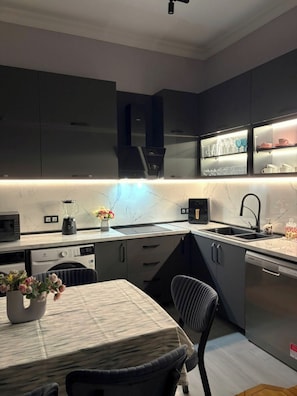 A modern kitchen with dark cabinetry, a built-in oven, and a countertop with a blender and flowers.