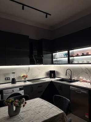 A modern kitchen with dark cabinetry, a marble countertop, a built-in oven, and a dishwasher.