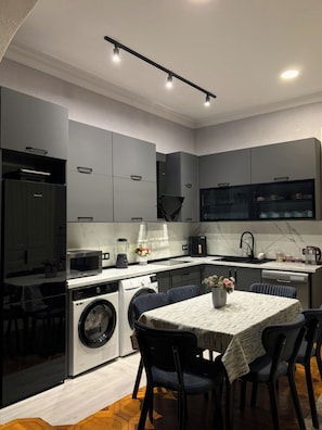 A modern kitchen with grey cabinets, a built-in oven, and a dining area with a table and chairs.