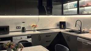 Una cocina moderna con armarios oscuros, encimera de mármol, horno empotrado y una zona de comedor con mesa y sillas.