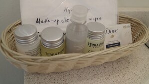 A wicker basket containing various skincare products including Terra Pure and Dove brands, along with a bag labeled "Make-up cleansers wipes".