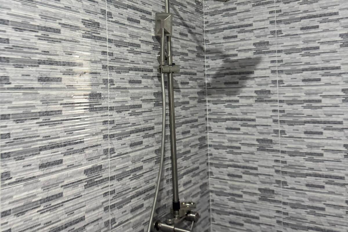 Ducha con cabezal de ducha de mano y grifo empotrado en una pared de baño con azulejos estampados.