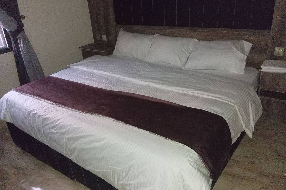 Una cama con ropa de cama blanca y marrón, un cabecero de madera y una mesita de noche con una lámpara.