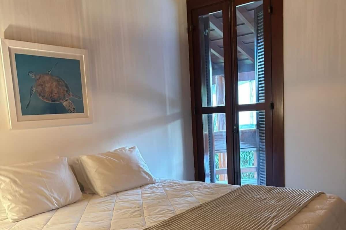 Een slaapkamer met een bed, een ingelijst schilderij van een schildpad en een raam met jaloezieën.