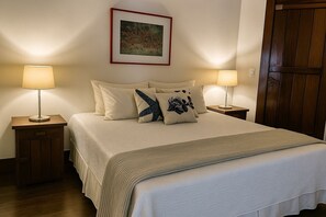 A neatly made bed with a beige comforter and pillows, two bedside tables with lamps, a framed artwork on the wall, and a wooden door. - 120 Hotel & Beach Club (Guaruja)