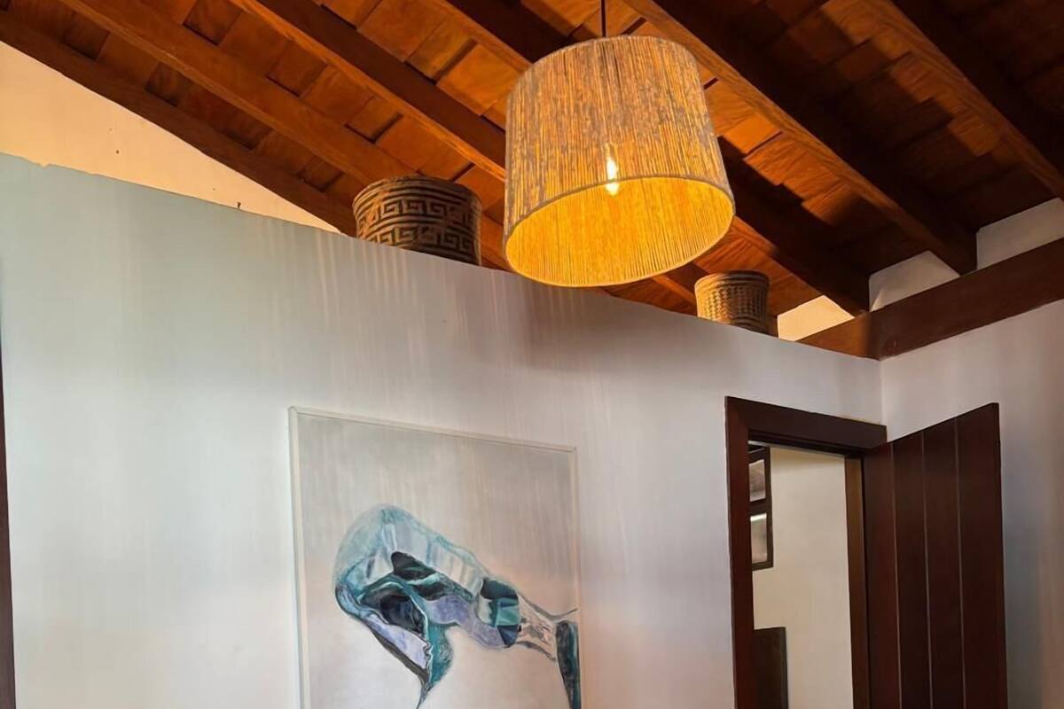 Een slaapkamer met een bed, nachtkastje, lamp, schilderij en een deur.