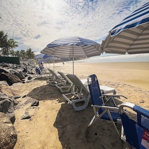 Na praia, areia branca, barracas de praia de cortesia, espreguiçadeiras