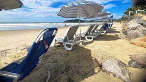 Une plage bordée de rangées de chaises longues et de parasols à rayures, un rivage sablonneux et une vue sur l’océan.